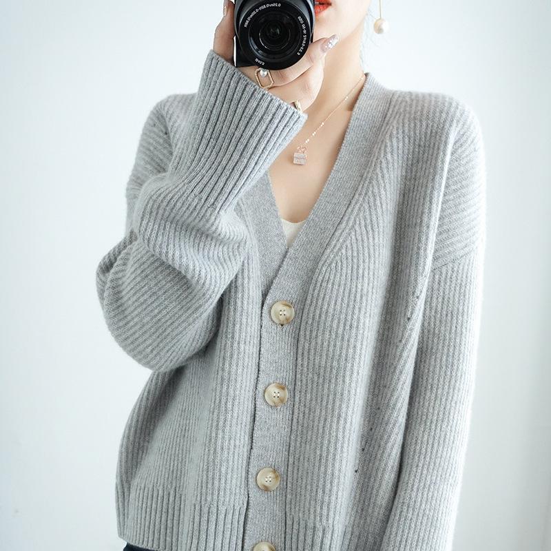 Femme portant un gilet ample boutonné en laine grise avec quatre boutons en bois et col en V, prise en photo de face.