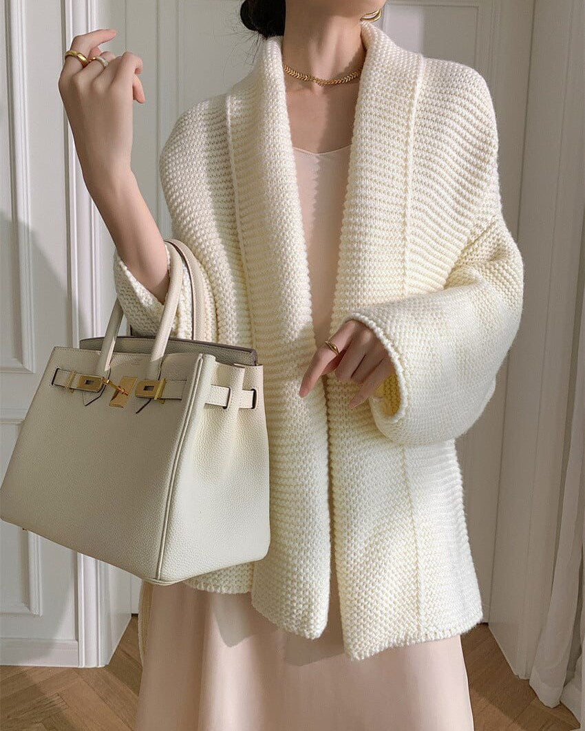 femme portant un élégant gilet blanc sans boutons hélia en maille large, associé à un sac à main crème chic et une robe beige