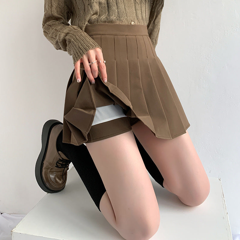 jupe plissée noire avec short intérieur visible, modèle louise portant des chaussures marron et un pull à manches longues beige