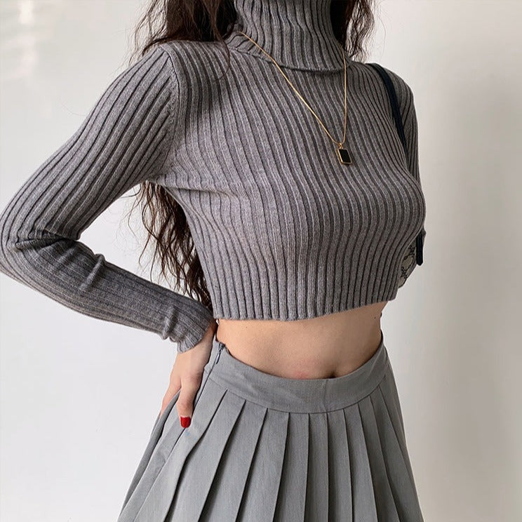 pull court col roulé pour femme en tricot gris, associé à une jupe plissée grise, look élégant et moderne
