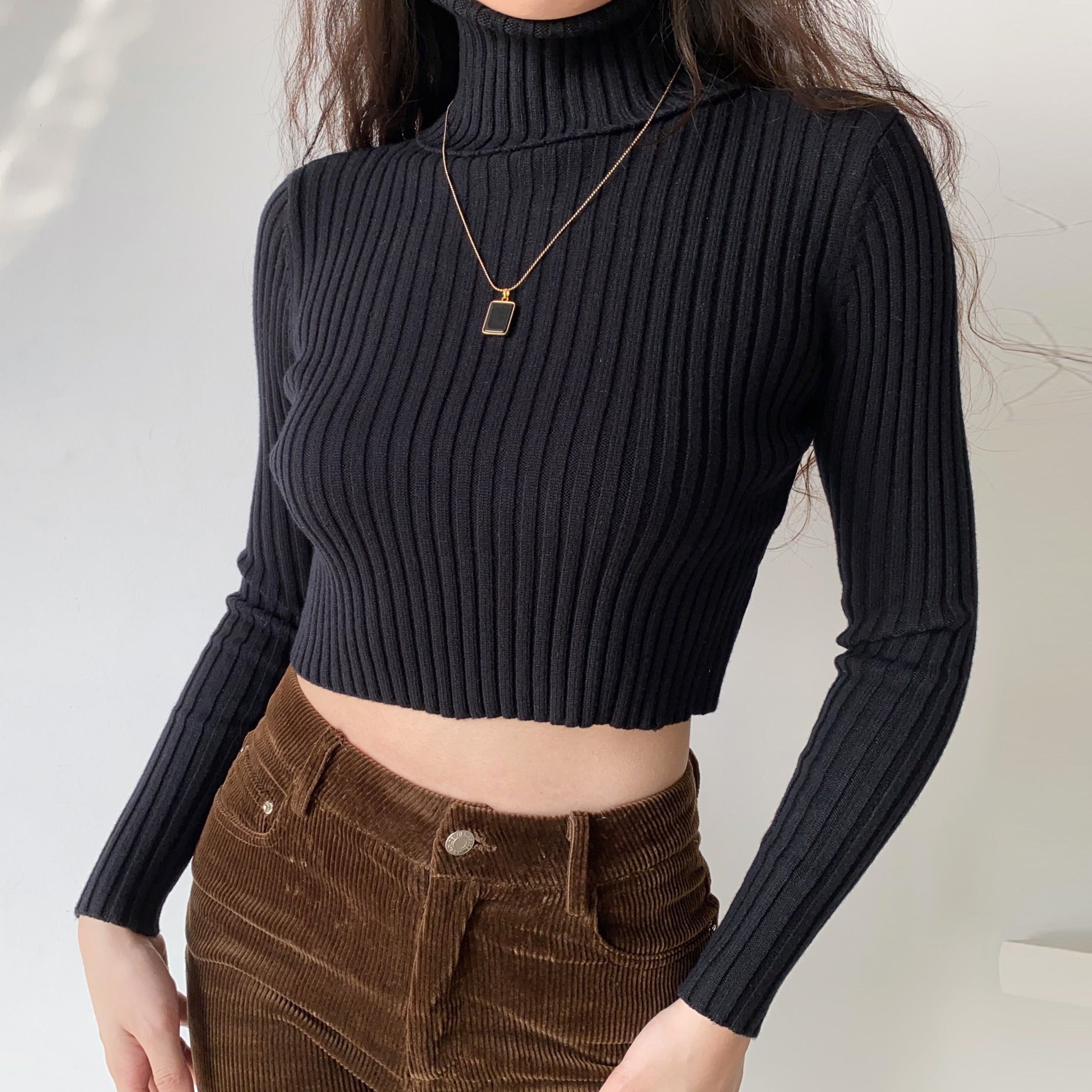 pull court col roulé noir pour femme avec manches longues et motif côtelé, porté avec un pantalon marron en velours côtelé