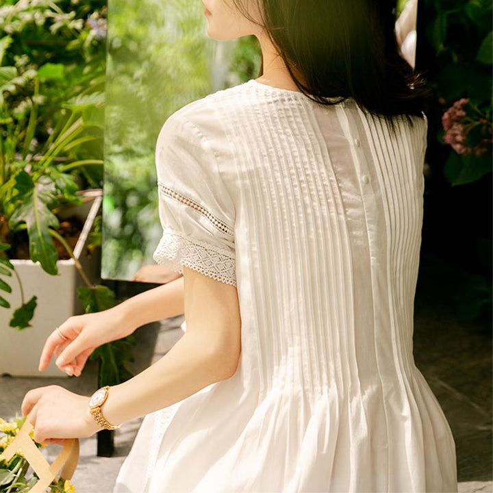 Jeune femme portant une robe blanche en coton avec des manches en dentelle, dos en vue dans un jardin verdoyant.