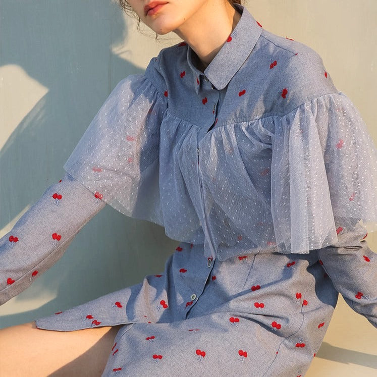 femme portant une robe chemise bleue avec des motifs de cerises rouges et des manches transparentes à volants