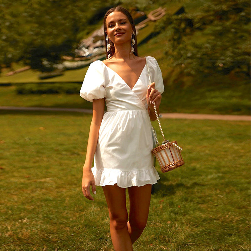 femme portant une robe blanche courte en lin avec poches pouffantes dans un jardin, accessoirisée d'un petit sac à bandoulière