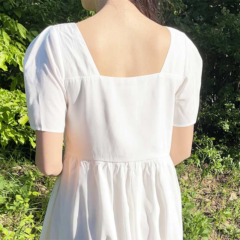 robe bohème blanche charlotte vue de dos avec encolure carrée et manches courtes dans un jardin verdoyant