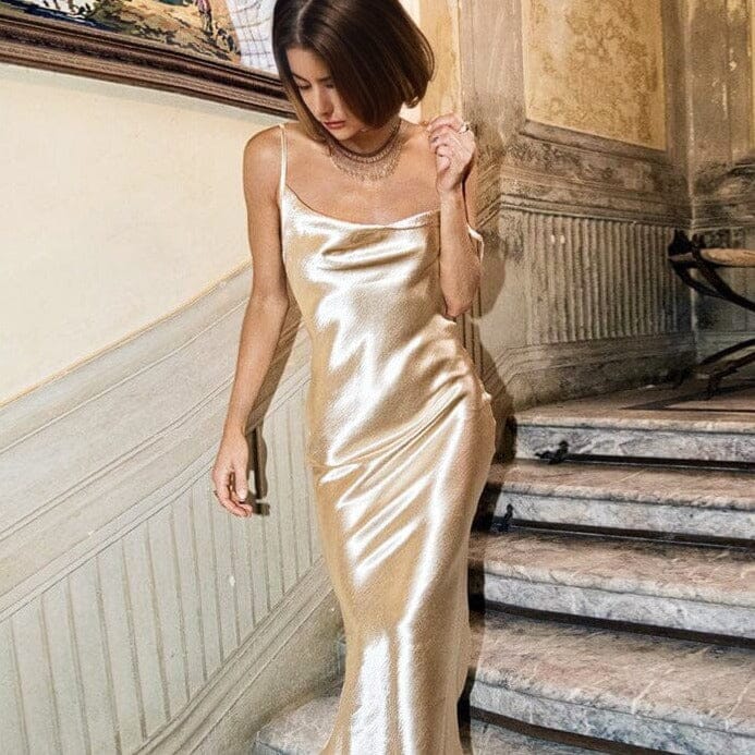 robe de soirée dos nu malena en satin doré portée par une femme descendant un escalier élégant et chic