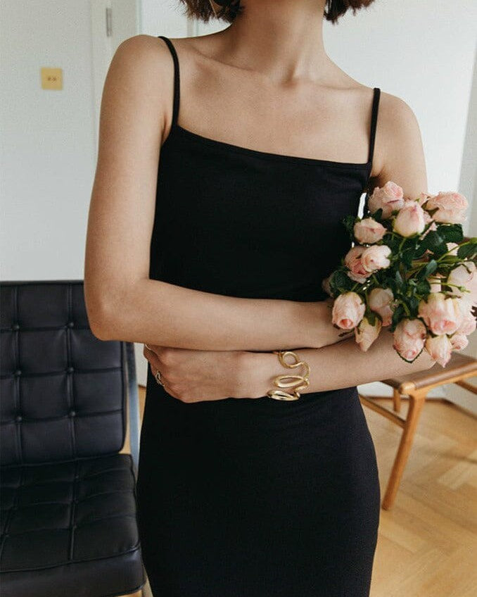 femme portant une robe noire dos nu, tenant un bouquet de fleurs roses, posant dans un salon élégant