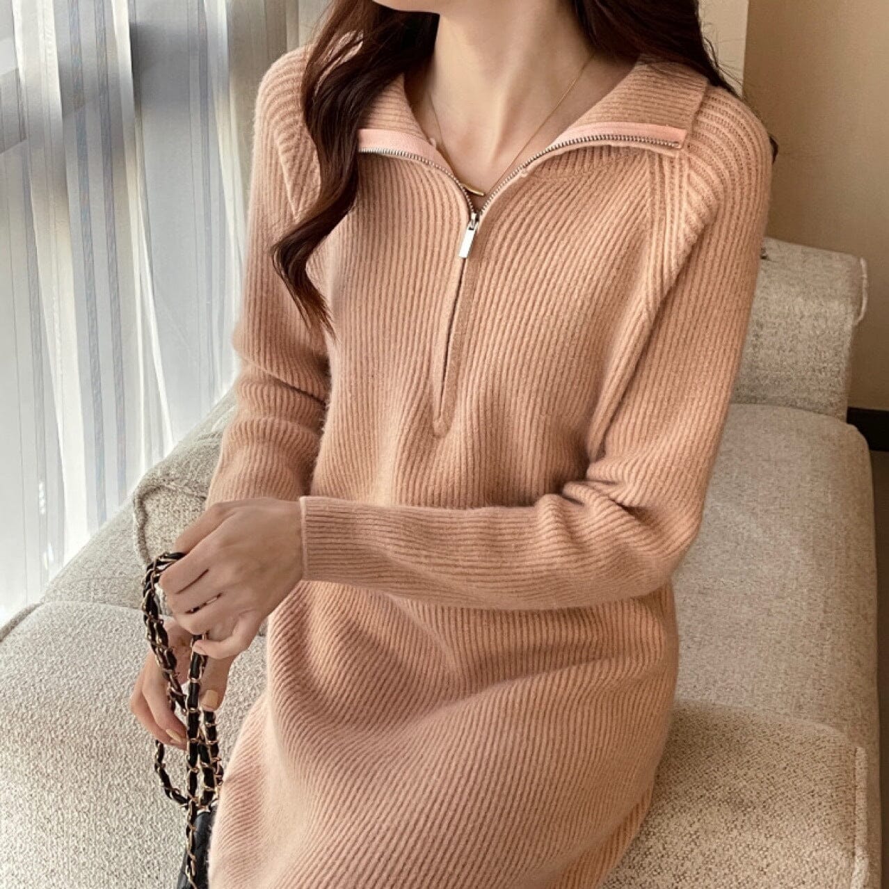 robe en laine longue beige avec col zip porté par une femme assise sur un canapé près d'une fenêtreosť