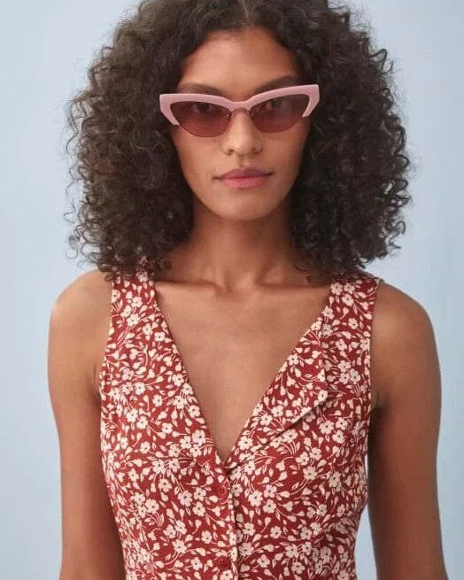 femme portant une robe rouge courte fleurie charlie avec des lunettes de soleil roses et cheveux bouclés