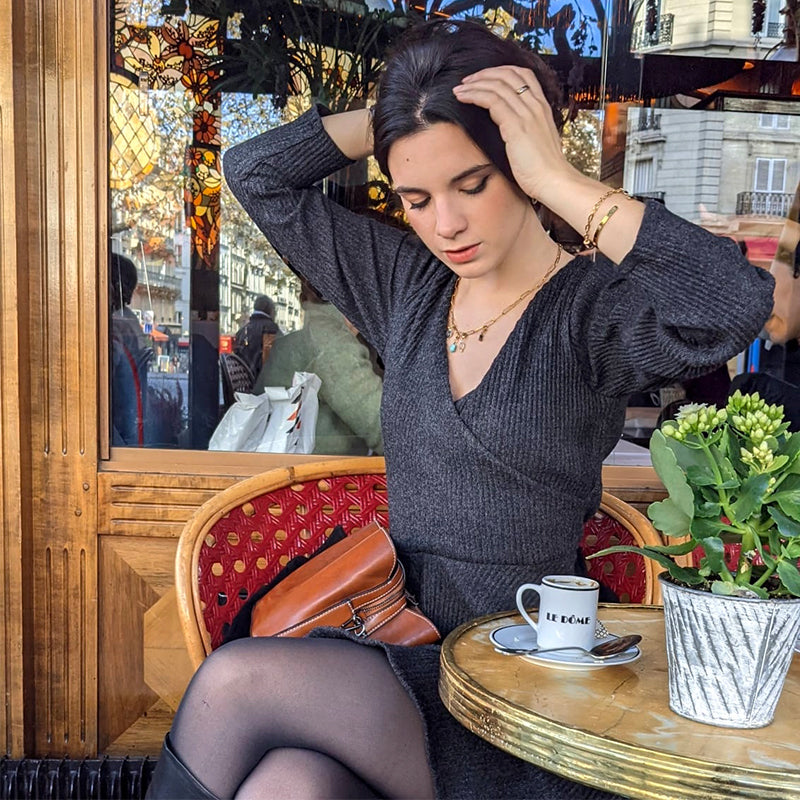 femme portant la robe pull cintrée oriane en laine grise assise à une table de café avec une tasse et une plante verte