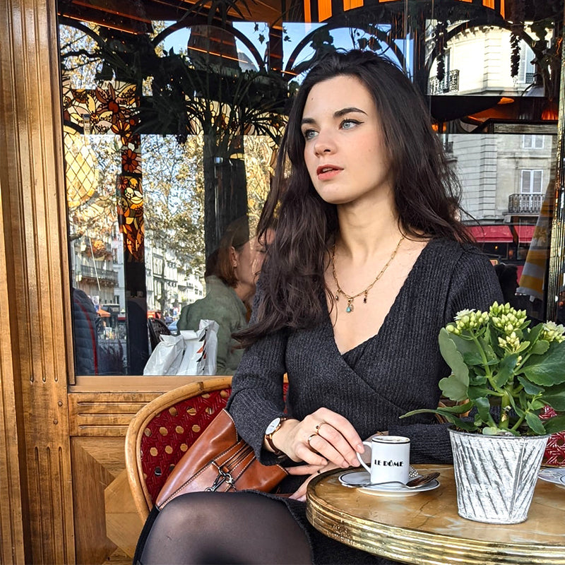 jeune femme portant une robe pull cintrée noire devant un café avec une tasse de café et une plante en pot