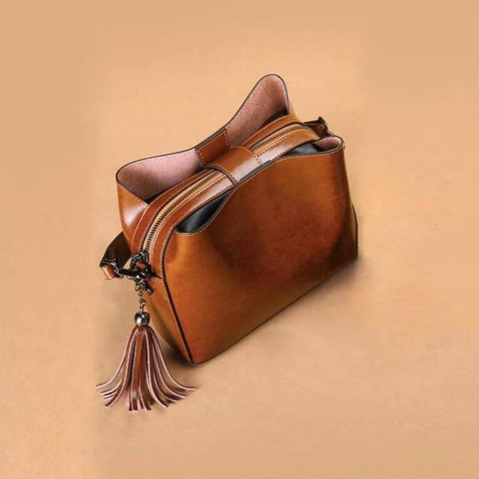 petit sac bandoulière en cuir marron avec pompon en décoration, idéal pour un usage quotidien et sorties élégantes