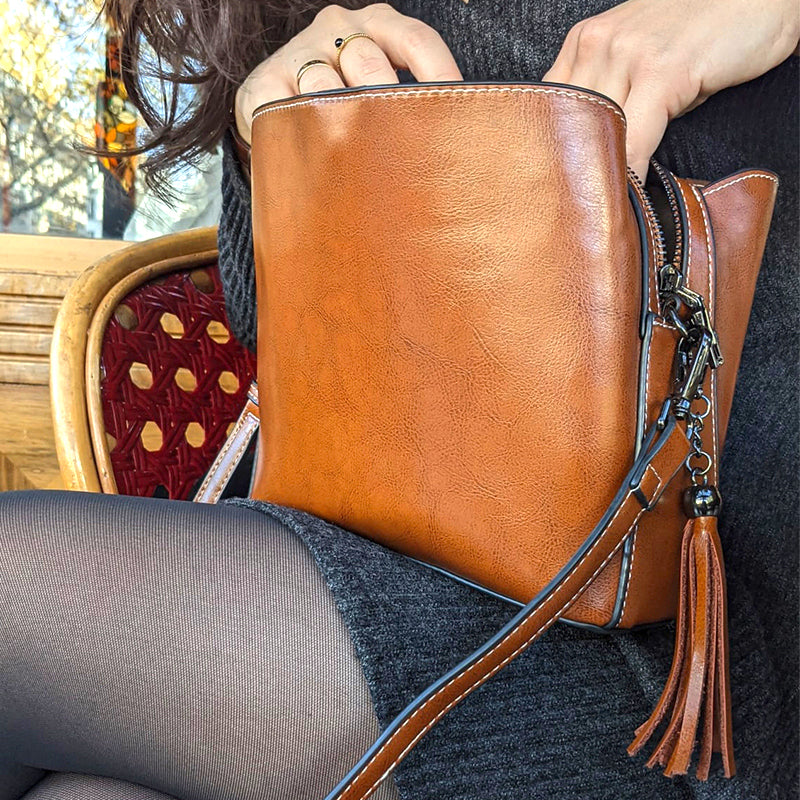 petit sac en bandoulière en cuir marron porté par une femme avec une robe grise, assise sur une chaise rouge